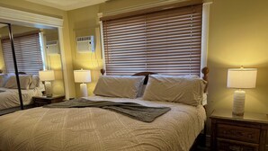 Ein Schlafzimmer mit Bett, Nachttischen, einer Lampe, einem Spiegel und einem Fenster mit Jalousien.