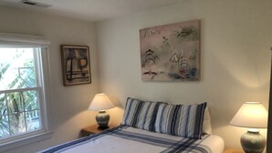 A neatly made bed with striped bedding, two bedside lamps, and artwork on the walls.