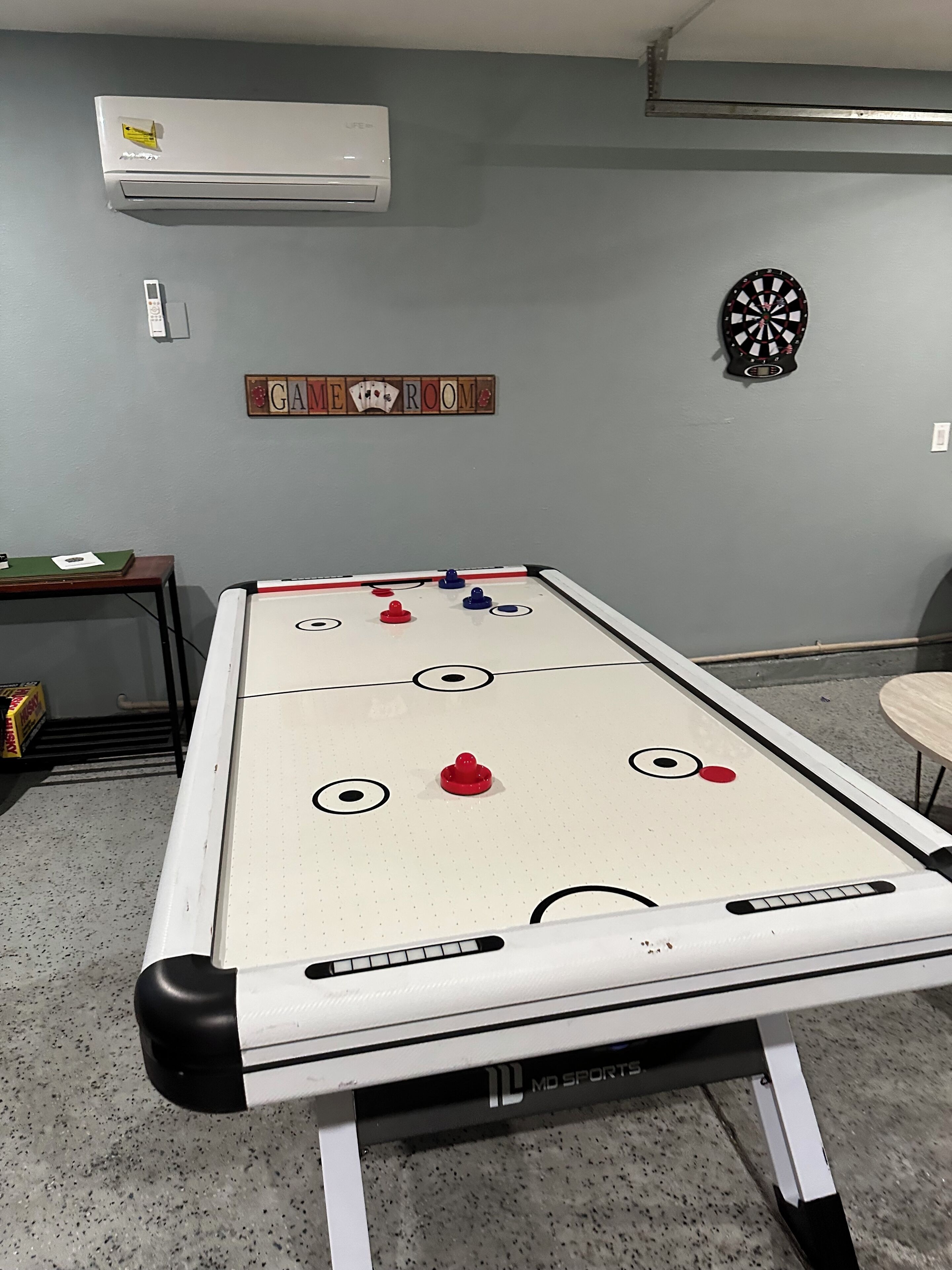 Una mesa de fútbolín en una sala con un dardo y un letrero que dice 'GAME ROOM'.