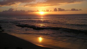 Un coucher de soleil sur l’océan, avec des vagues qui se brisent sur une plage.