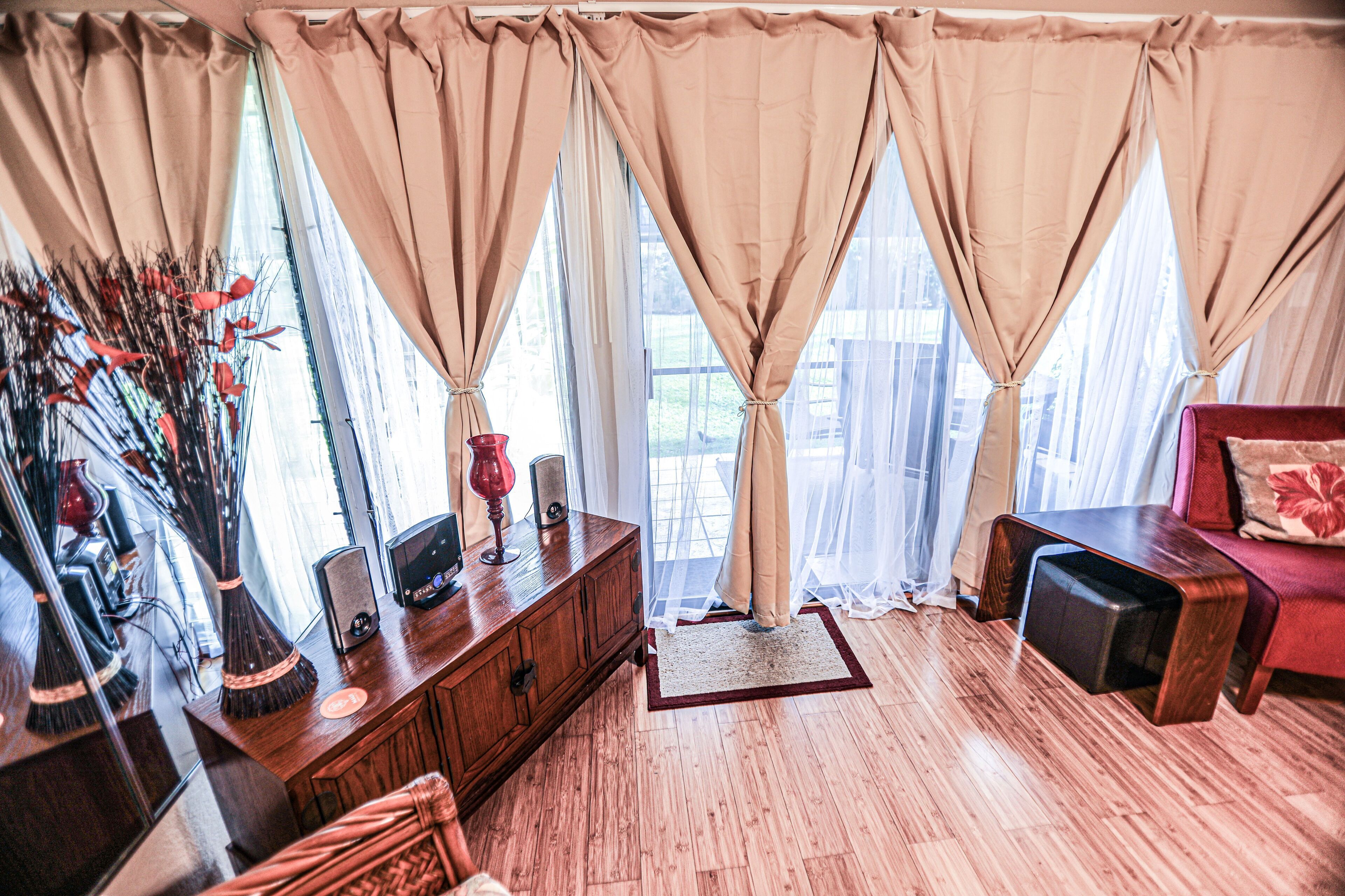 A room with a wooden floor, a wooden cabinet, a red chair, and a window with beige curtains.