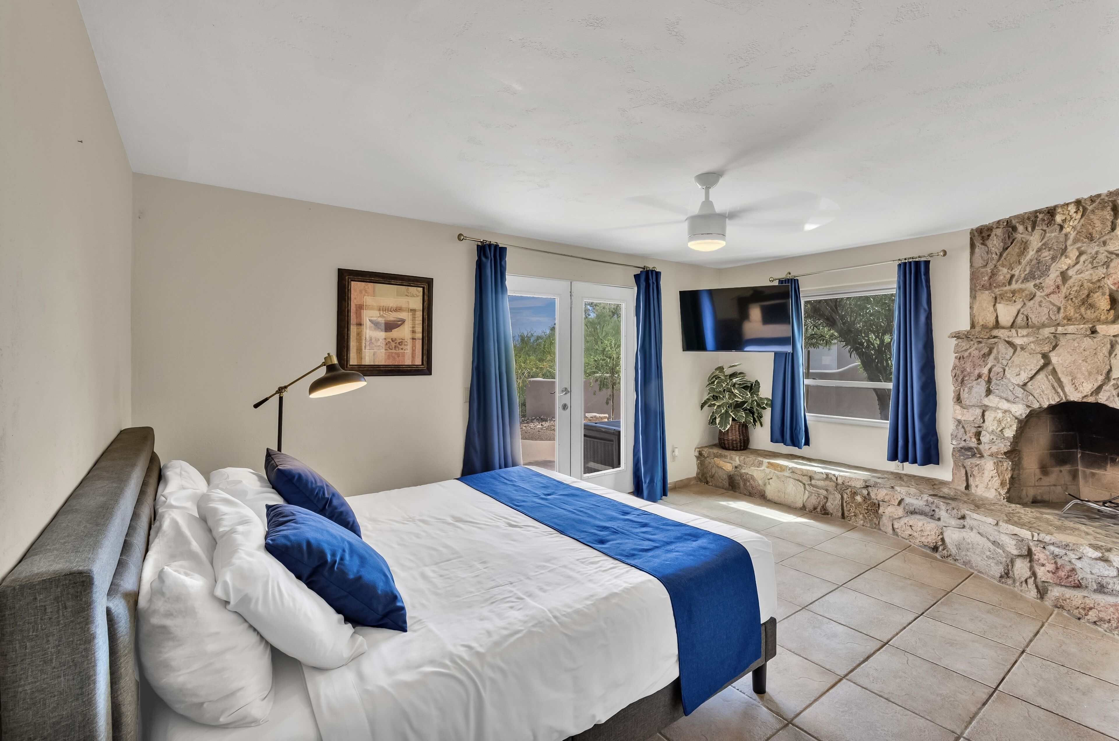 A bedroom with a bed, a stone fireplace, a TV, and a balcony with curtains.