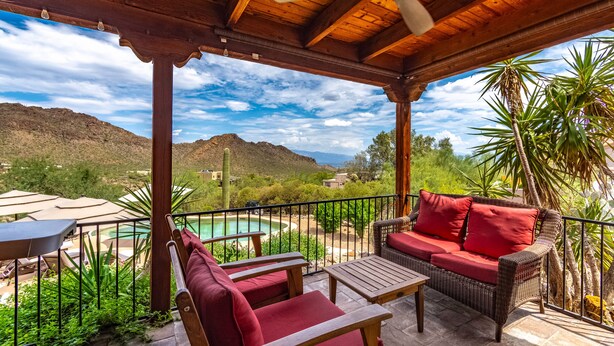 Eine überdachte Terrasse mit Pool, Korbmöbeln und Blick auf die Berge.