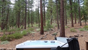 A hot tub in a forested area with tall pine trees and a wooden deck. - Serene Vistas at Northstar (Truckee)