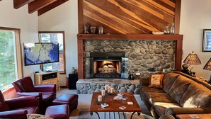 A cozy living room with a stone fireplace, leather furniture, and a television. - Serene Vistas at Northstar (Truckee)