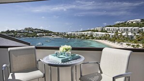 Un balcón con dos sillas y una mesa, con vista a una playa con barcos y una zona turística.