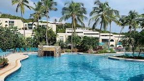 Piscina de resort con una cascada de piedra, rodeada de palmeras y sillas de descanso.