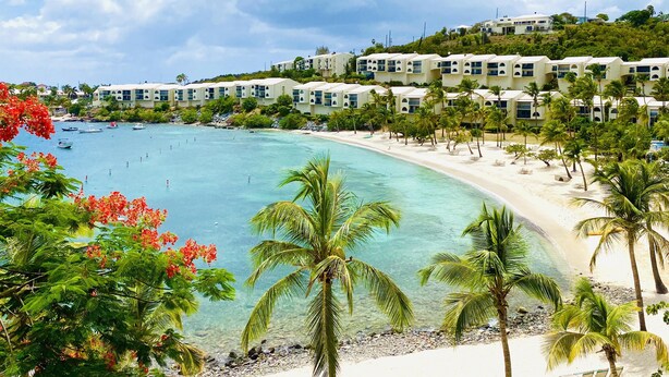 Un resort costero con villas frente a la playa, aguas turquesas cristalinas y palmeras.