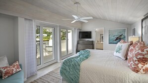 Un dormitorio con una cama grande, televisión, ventilador de techo y puerta corrediza de vidrio que da a un área exterior.