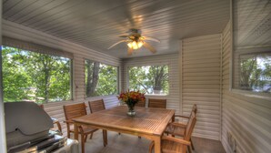 A covered patio with a wooden table and chairs, a ceiling fan, and a grill.
