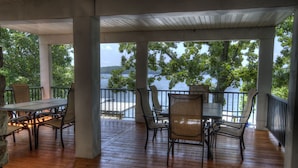 A covered outdoor area with a wooden deck, a table, and chairs. - 8500 sf, Sleeps 48 in beds, Pool, Hot Tub, Game Rm, 300 ft lake front, In town (Osage Beach)