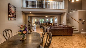 A spacious living area with a wooden herringbone floor, a brown leather sofa, and a dining table with chairs.