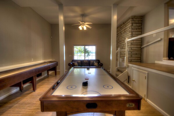 A pool table in a room with a ceiling fan, a window, and a staircase.