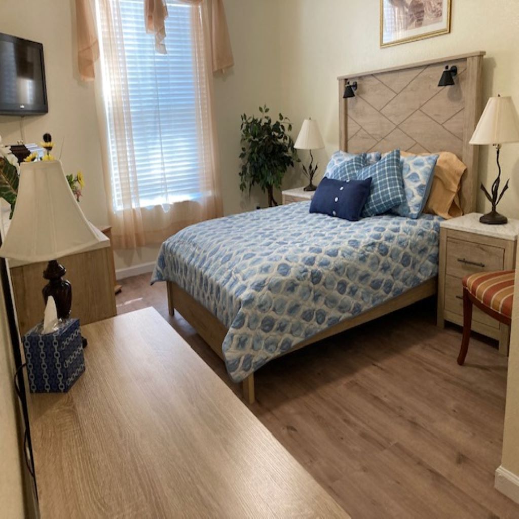 A bedroom with a bed, bedside tables, a lamp, a plant, and a television on the wall.