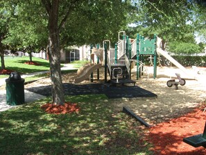 Children can play on the slide, climbing structure, and ride tricycles in this well-maintained playground surrounded by trees.