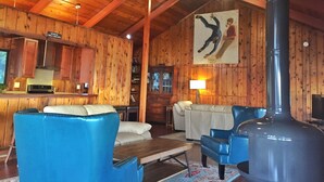 A wooden interior with a high ceiling, a large fireplace, blue leather chairs, a sofa, and a painting of a person falling.
