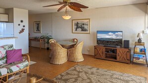 A living room with a television, wooden entertainment unit, wicker furniture, and a ceiling fan. - Aloha Kai-Private Ocean View Condo in Kihei Steps to the Beach! (Kihei)