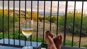 A balcony with a glass table, a glass of white wine, and a person's feet. - Aloha Kai-Private Ocean View Condo in Kihei Steps to the Beach! (Kihei)