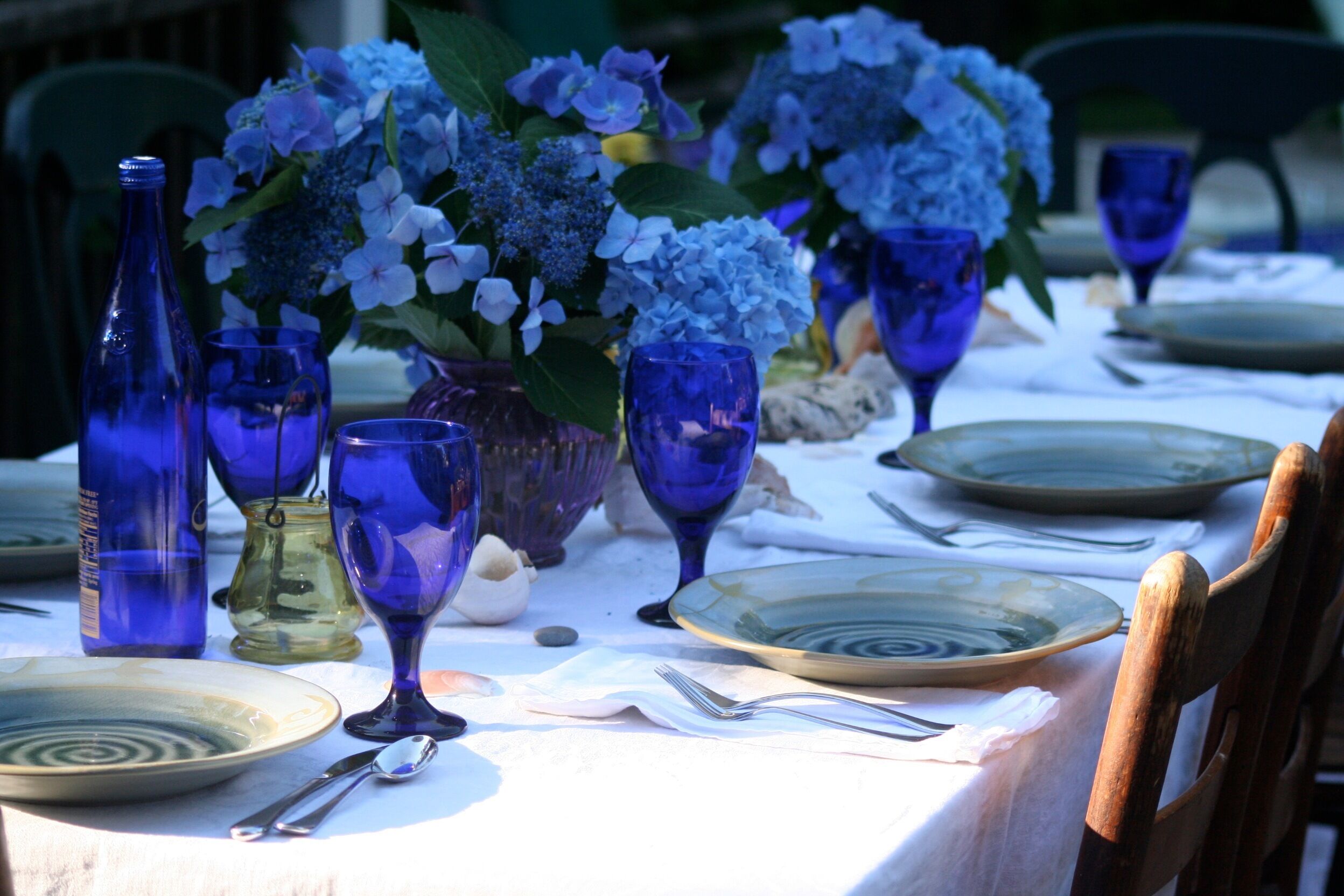 A table set with blue glassware, plates, and a vase of flowers.
