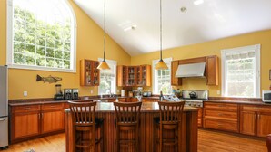 A spacious kitchen with wooden cabinets, a large island with bar stools, and a fish decoration on the wall. - Luxury 7 BR, 4 BA w/ Unique 60 ft Pool, .4 Miles to Beach (Orleans)