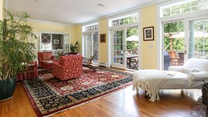 A spacious living room with hardwood floors, a large red and blue patterned rug, a white sofa, a red patterned armchair, and a potted plant. - Luxury 7 BR, 4 BA w/ Unique 60 ft Pool, .4 Miles to Beach (Orleans)