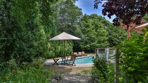 A backyard with a swimming pool, surrounded by lush greenery and a pergola with an umbrella. - Luxury 7 BR, 4 BA w/ Unique 60 ft Pool, .4 Miles to Beach (Orleans)