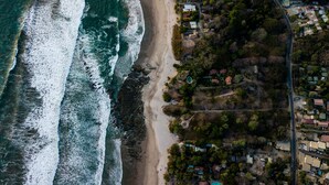 Une vue aérienne d’une zone côtière avec une plage, des maisons et une route.
