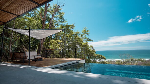 Un espace piscine extérieur moderne, doté d’une terrasse en bois, de sièges et offrant une vue sur l’océan.