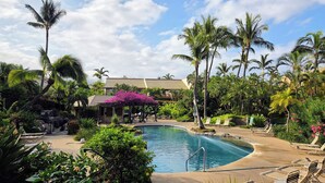 A pool area with lounge chairs, palm trees, and a building with a tiled roof. - Rare No-Stairs Ocean View Condo ~ Maui Kamaole (Kihei)