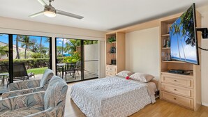 A bedroom with a bed, a TV, a ceiling fan, a sliding glass door to a balcony, and a wooden dresser. - Rare No-Stairs Ocean View Condo ~ Maui Kamaole (Kihei)