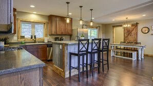 A spacious kitchen with wooden cabinets, a central island with bar stools, and pendant lighting. - Lazy Dog Lodge, Hot Tub, AC & Activities Near Black Hills (Lead)
