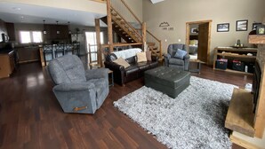 A spacious living area with a high ceiling, a wooden staircase, and a kitchen in the background. - Lazy Dog Lodge, Hot Tub, AC & Activities Near Black Hills (Lead)