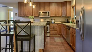 A kitchen with wooden cabinets, a stainless steel refrigerator, a microwave, and a dining area with chairs and a table. - Lazy Dog Lodge, Hot Tub, AC & Activities Near Black Hills (Lead)