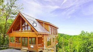 Une cabane en bois dotée d’un balcon, de grandes fenêtres et offrant une vue sur une zone boisée.