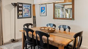 Un comedor con una mesa de madera, sillas negras, un bol de aperitivos, cuadros enmarcados y un espejo en la pared.