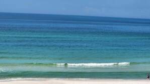 Una playa con agua azul cristalina y una persona caminando por la orilla.