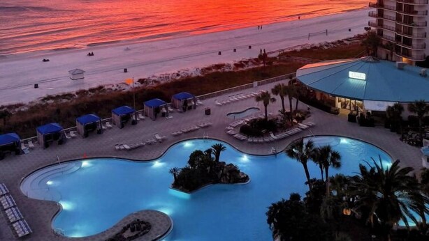Un resort con zona de piscina, acceso a la playa y vistas al atardecer sobre el océano.