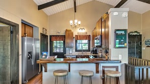 A kitchen with a central island, wooden bar stools, a refrigerator, a coffee maker, and a sign that says "FRESH EGGS".