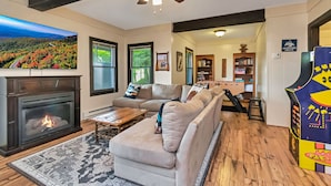 A living room with a fireplace, a sofa, a coffee table, and a view of a scenic landscape through the windows.