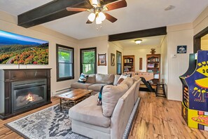 A living room with a fireplace, a sofa, a coffee table, and a view of a scenic landscape through the windows.