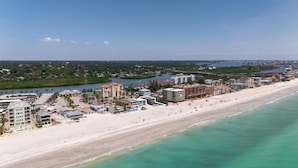 Vue aérienne d’une zone côtière avec une vaste plage de sable, un port de plaisance et divers bâtiments, notamment des hôtels et des immeubles d’habitation.