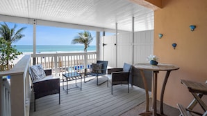 Un espace extérieur abrité, avec vue sur la plage, comprenant une table et des chaises, une petite table ronde ornée d’un vase et une rambarde blanche.