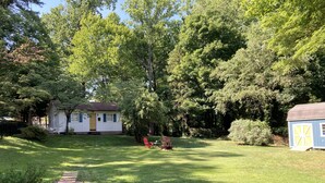 A backyard with a lawn, a red chair, and a small shed. - Relaxing Cottage close to everything! Perfect for 2!Wi-Fi, Keurig,Outside space! (Greensboro)