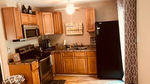 A compact kitchen with wooden cabinets, a black refrigerator, a microwave, and a coffee maker. - Relaxing Cottage close to everything! Perfect for 2!Wi-Fi, Keurig,Outside space! (Greensboro)