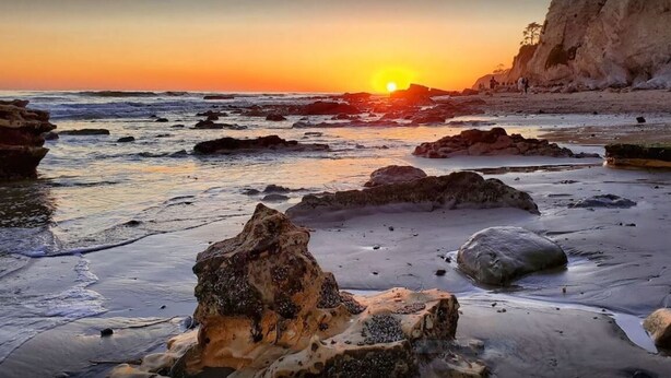 Una playa con rocas y un atardecer.