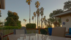 Un patio con mesa y sillas, rodeado por una valla de madera y palmeras.