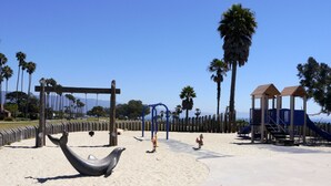Un parque infantil en la playa con columpios, un tobogán y una escultura de delfín.