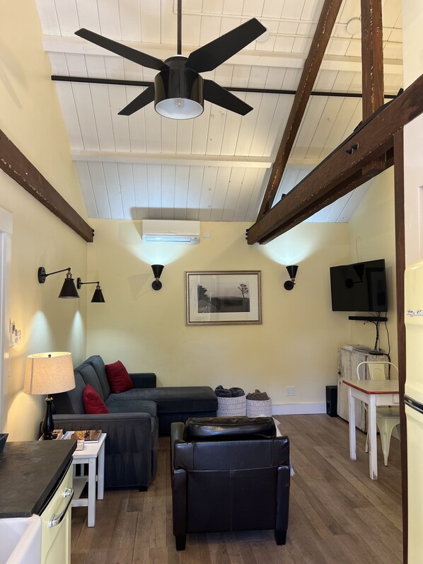 En stue med ventilator, sofa, sofabord, fjernsyn og et spiseområde med bord og stole.