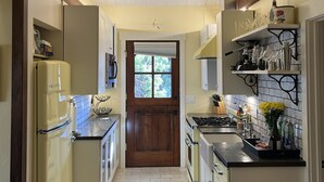 Una cocina estrecha con una puerta central, un ventilador de techo, luces colgantes y un refrigerador a la izquierda.