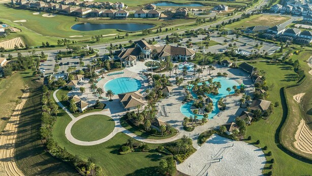 Vue aérienne d’un complexe hôtelier avec un parcours de golf, plusieurs piscines, des pelouses bien entretenues et des immeubles résidentiels.